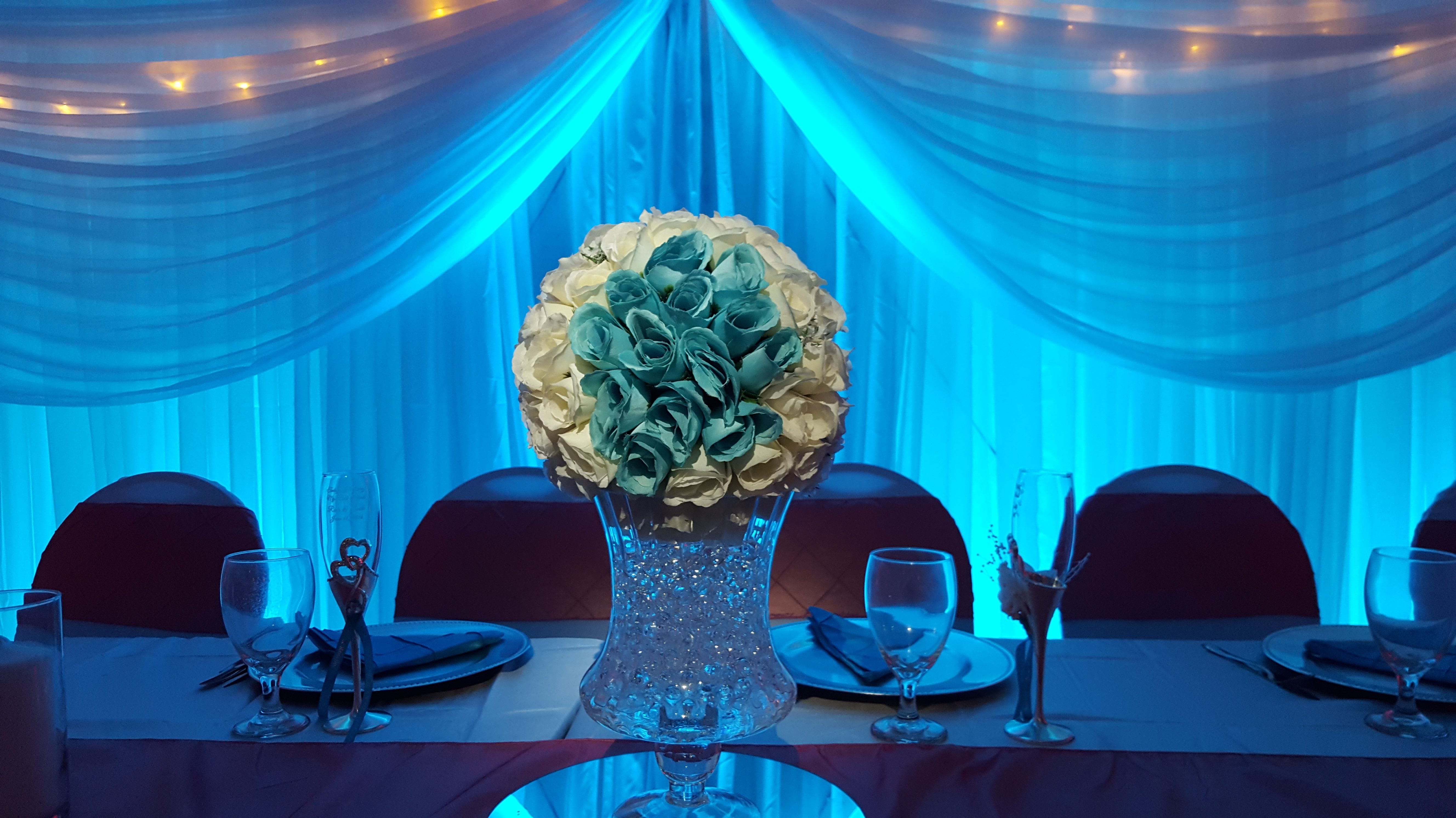 Head table backdrop lit in blue with flowers highlighted by pin spots.