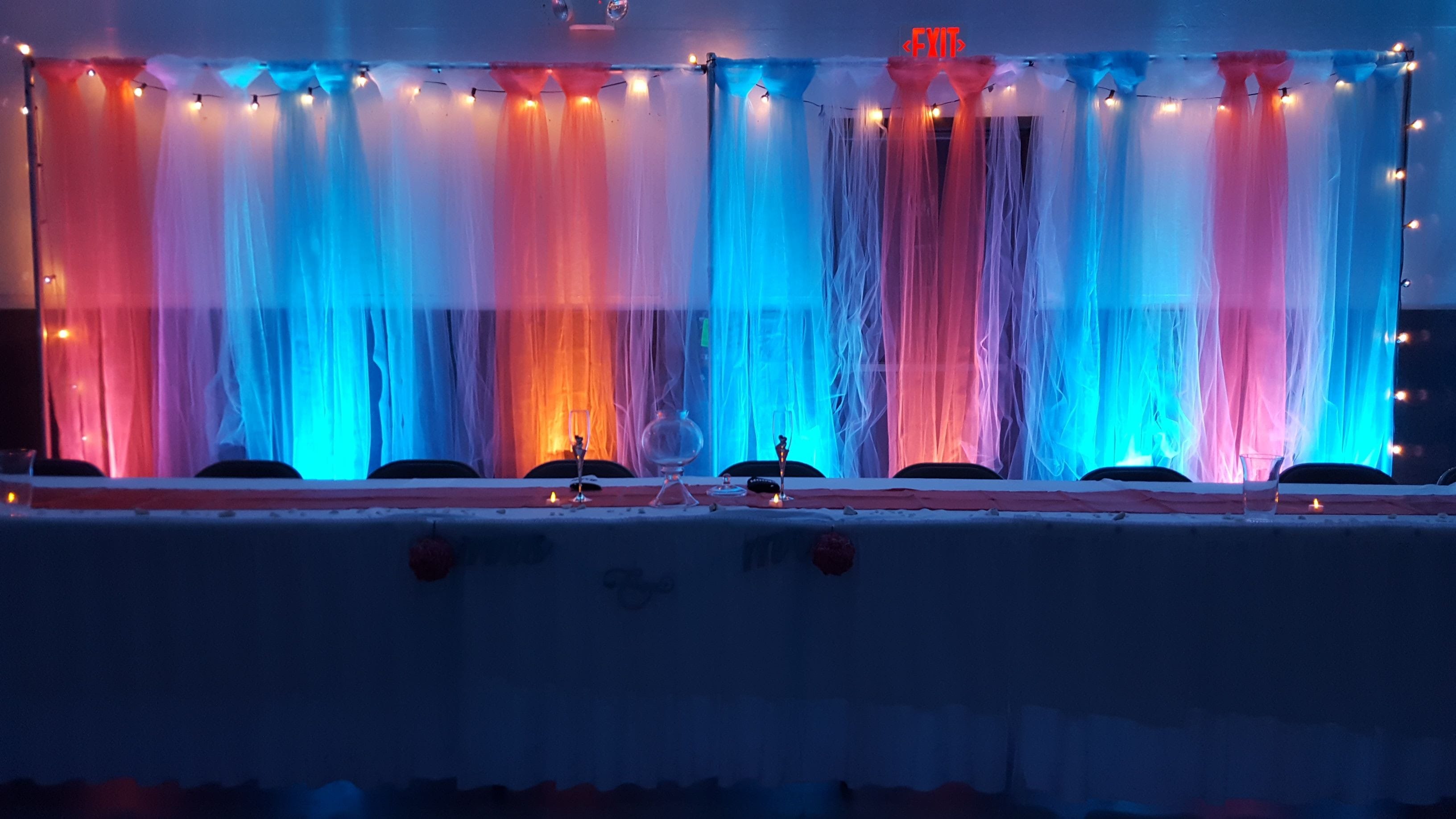 wedding lighting with teal and coral up lighting on a head table backdrop.